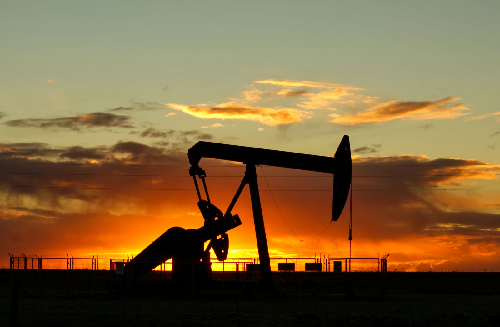 An oil pumpjack silhouetted against an orange sunset