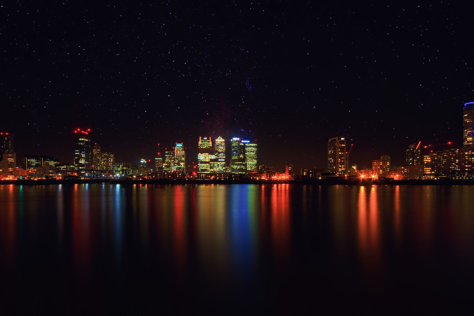 An illuminated city skyline mirrored in water at night